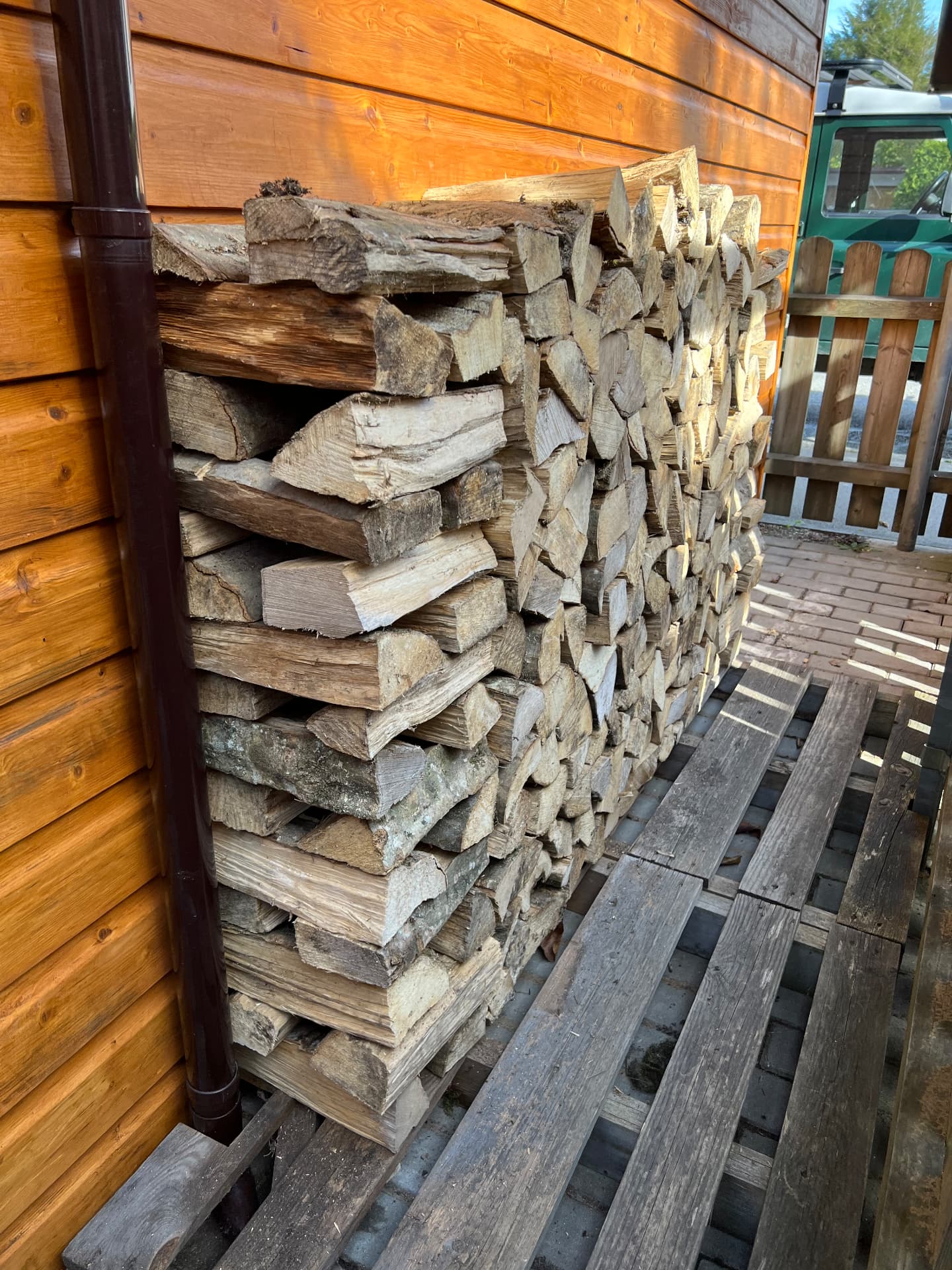 Sauber gestapeltes Brennholz an einer Holzwand unter dem Carport
